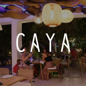 Outdoor dining at Caya restaurant featuring cozy lighting, woven decor, and lush greenery, providing a modern and relaxing ambiance for guests.